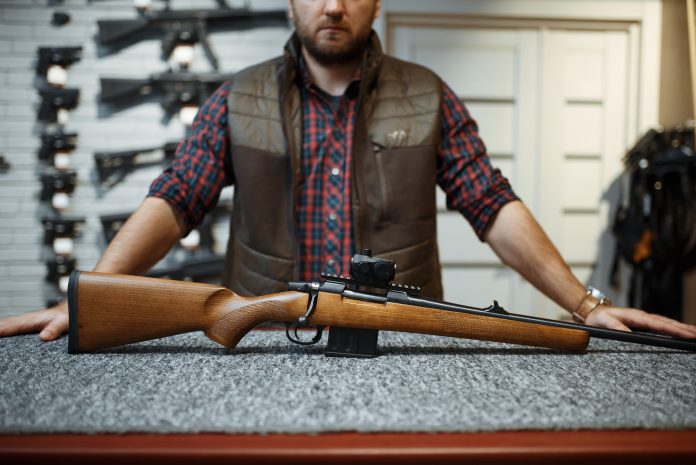 Man,With,Rifle,Standing,At,Counter,In,Gun,Shop